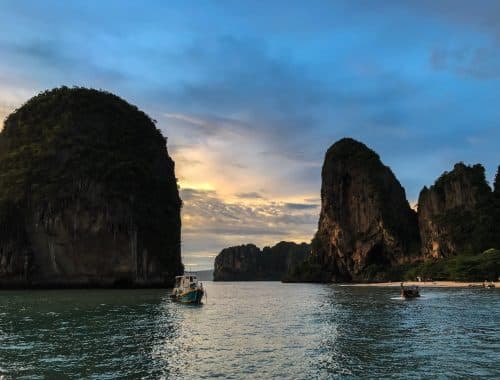 white and blue boat on sea near brown rock formation during daytime